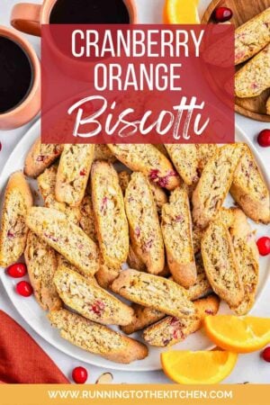 Cranberry orange biscotti recipe on a plate with oranges, cranberries and almonds scattered about.