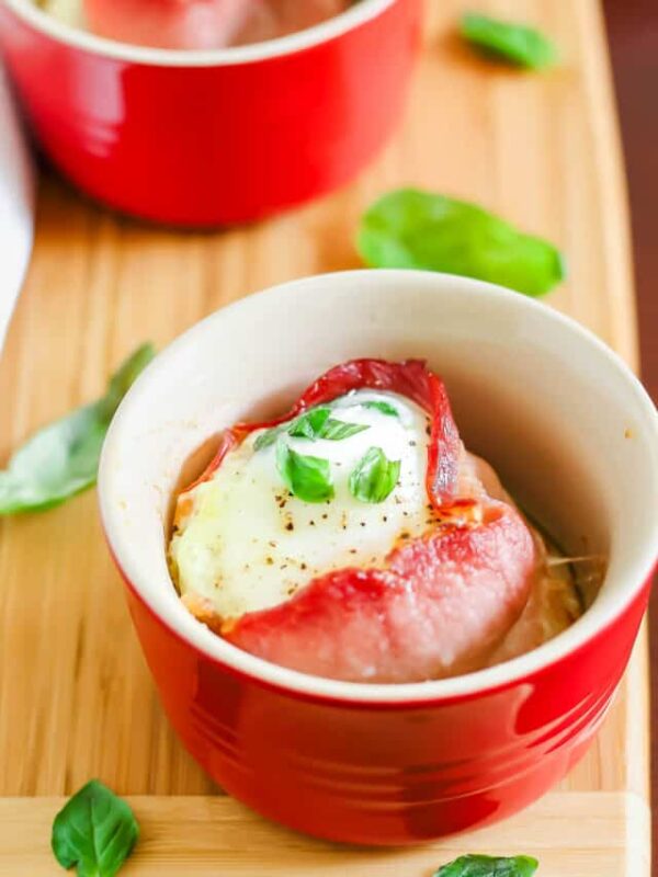 Bacon egg cups with basil on a wooden cutting board.