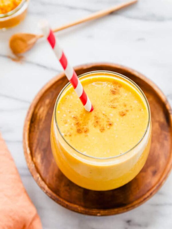 5-ingredient banana pumpkin smoothie in a glass with a red striped straw with cinnamon and pumpkin puree in the background.