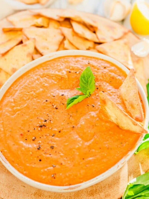 A bowl of tomato and basil dip with crackers.