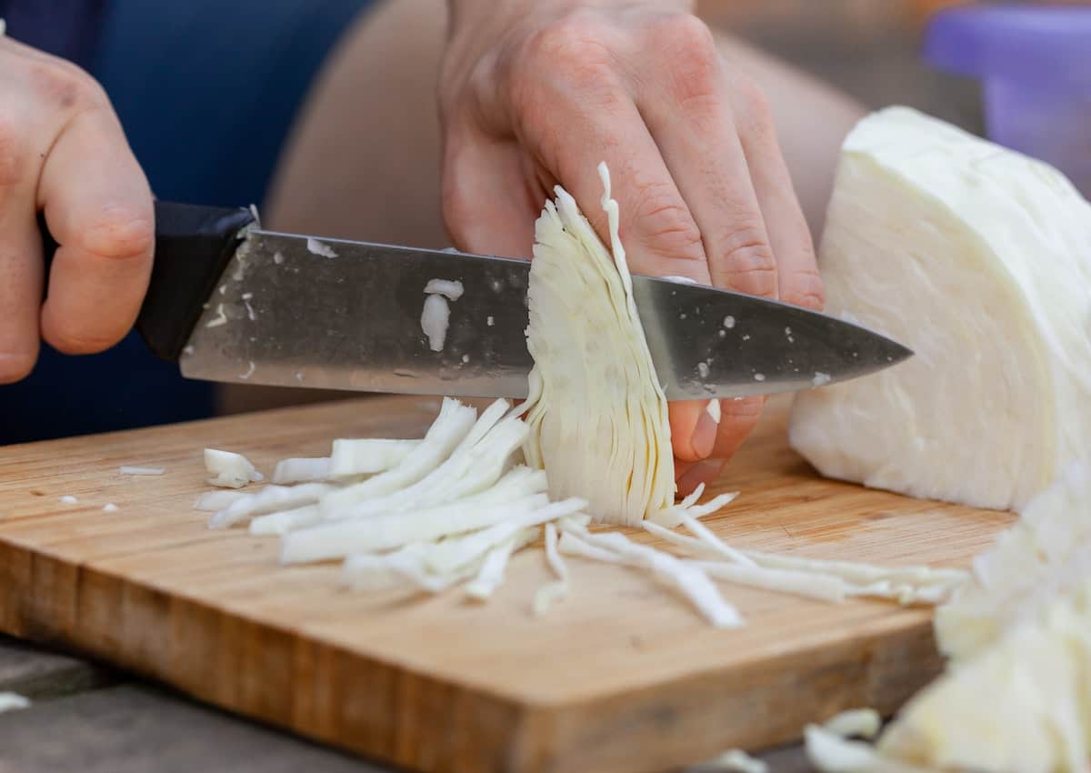 Thinly slicing cabbage on a cutting board.