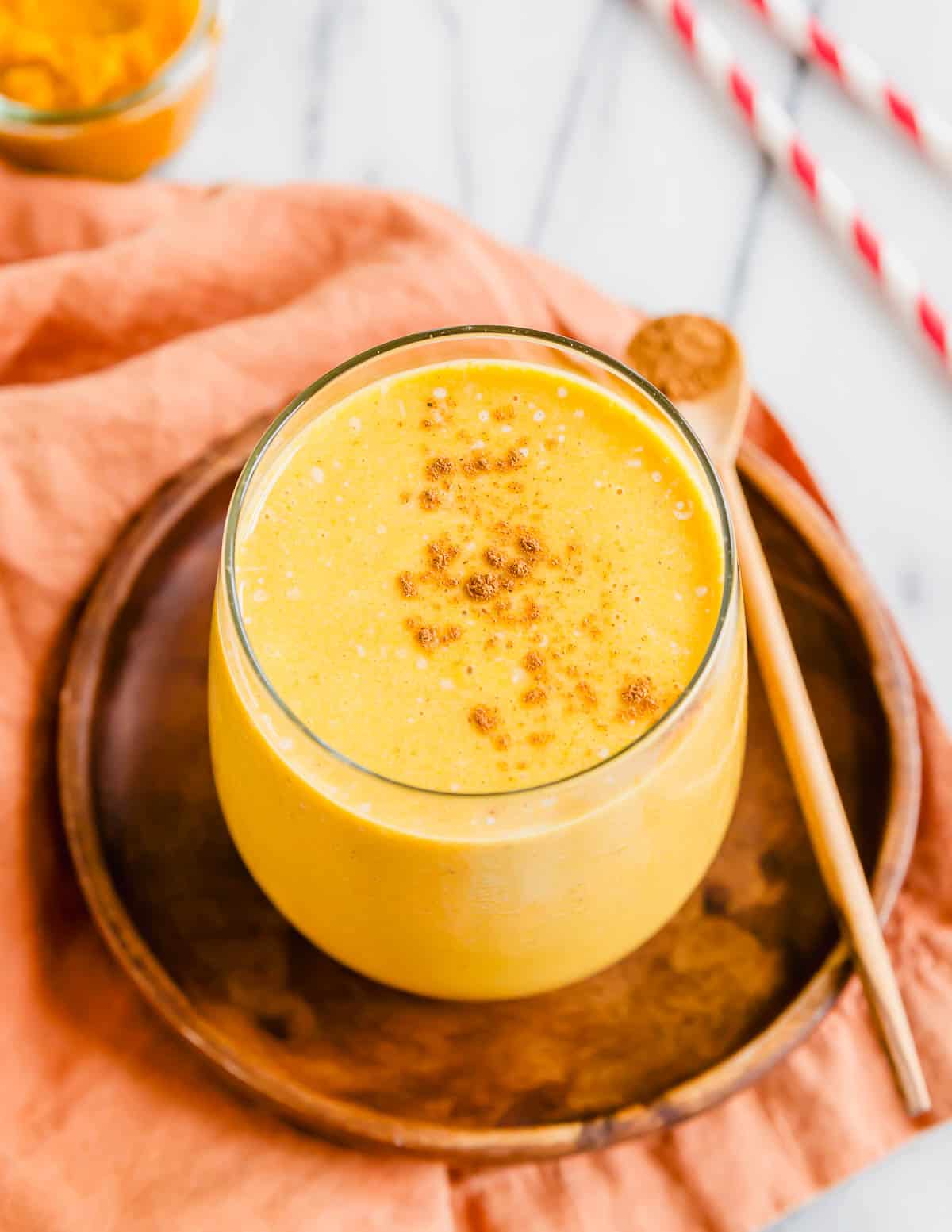 Creamy pumpkin banana smoothie with cinnamon in a glass on a wooden plate.