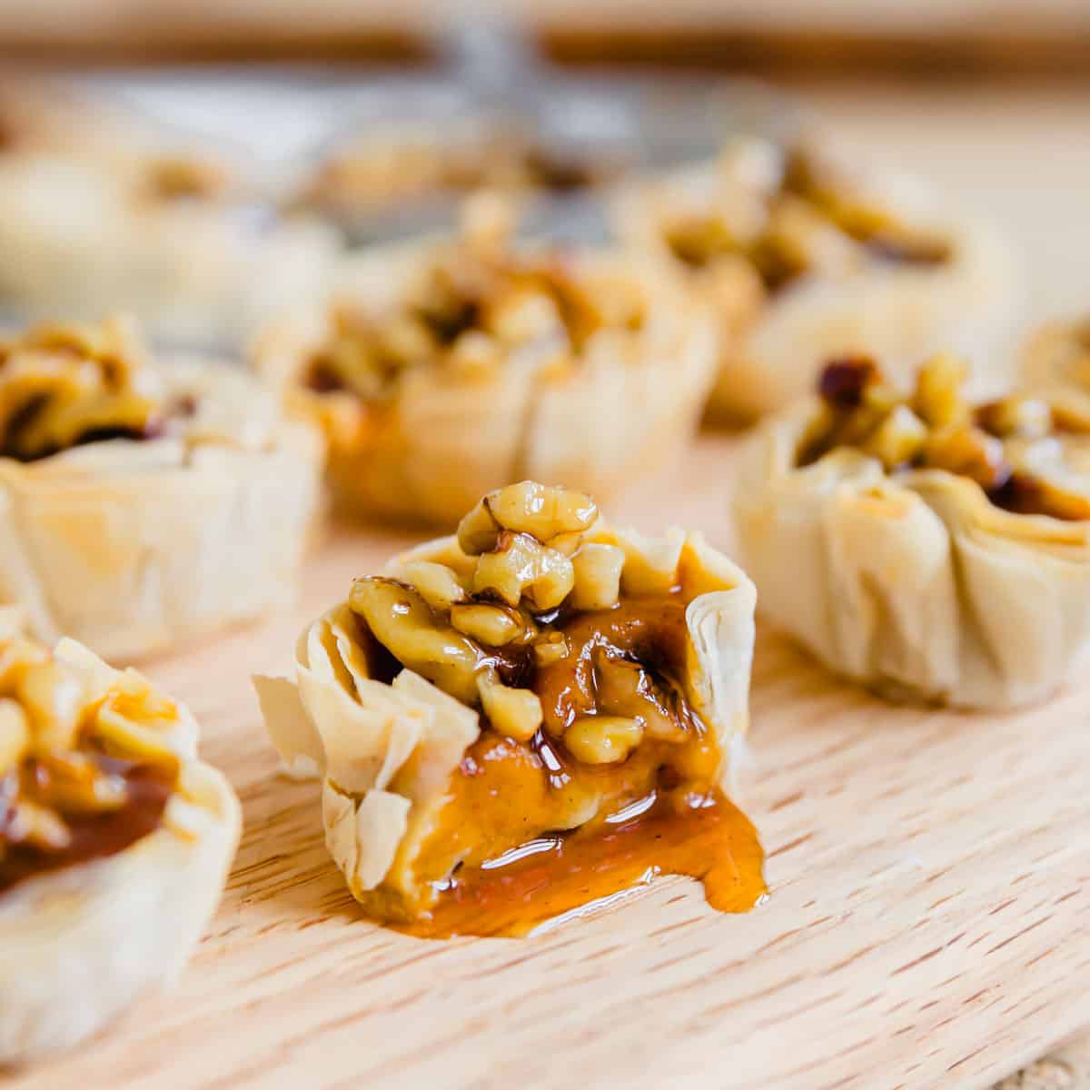 Pumpkin pie bite cut in half on a cutting board with walnuts and maple syrup topping.