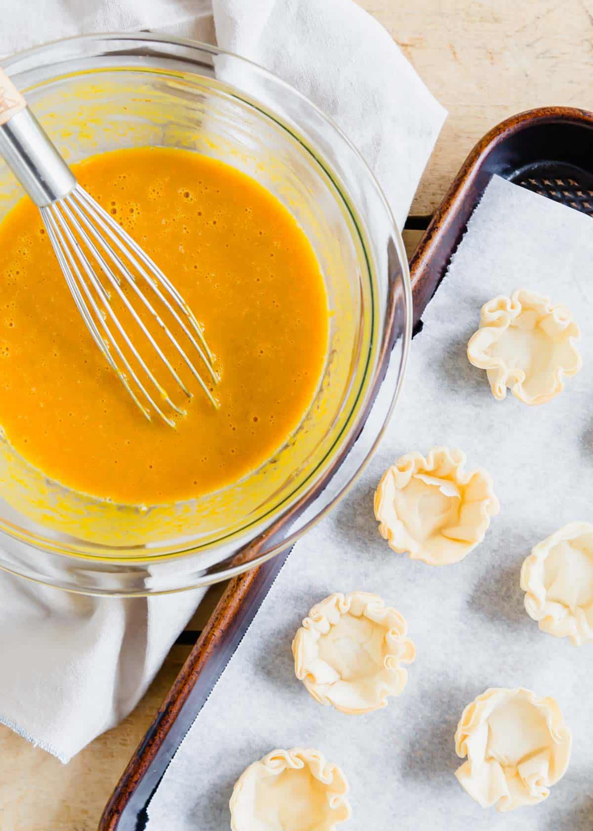 Pumpkin pie batter in a glass bowl with mini phyllo dough shells on a baking sheet.