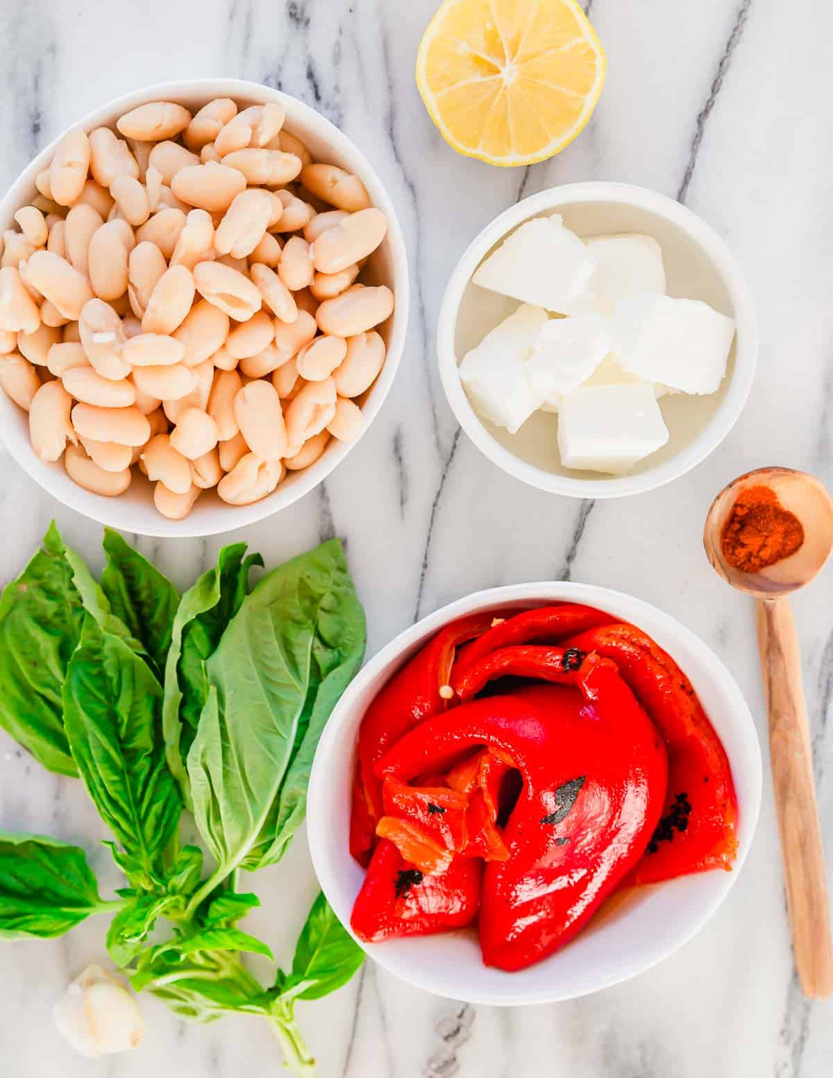 Roasted red peppers, white beans, feta, lemon, basil and smoked paprika in small bowls on a marble surface.