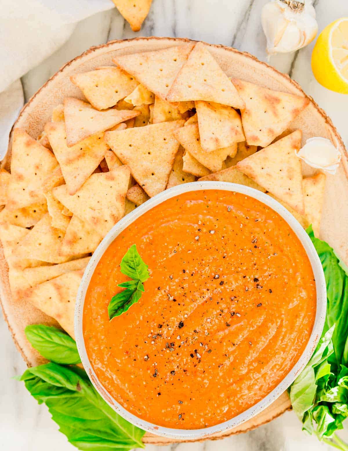 Creamy feta roasted red pepper dip recipe in a bowl garnished with basil with crackers scattered around it.