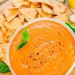 Overhead shot of roasted red pepper dip recipe in a bowl with pita chips around it.