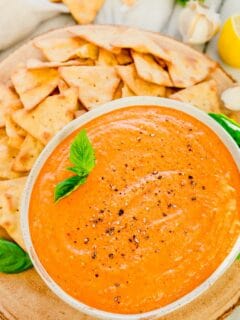 Overhead shot of roasted red pepper dip recipe in a bowl with pita chips around it.