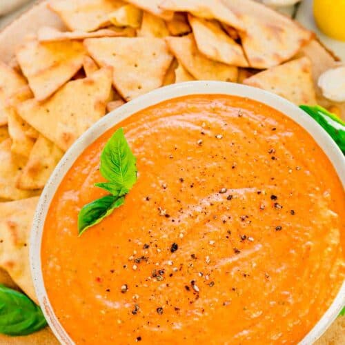 Overhead shot of roasted red pepper dip recipe in a bowl with pita chips around it.