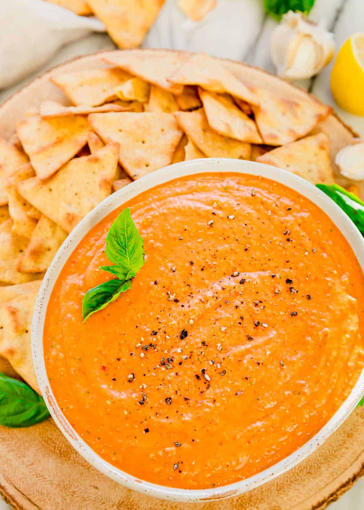 Overhead shot of roasted red pepper dip recipe in a bowl with pita chips around it.