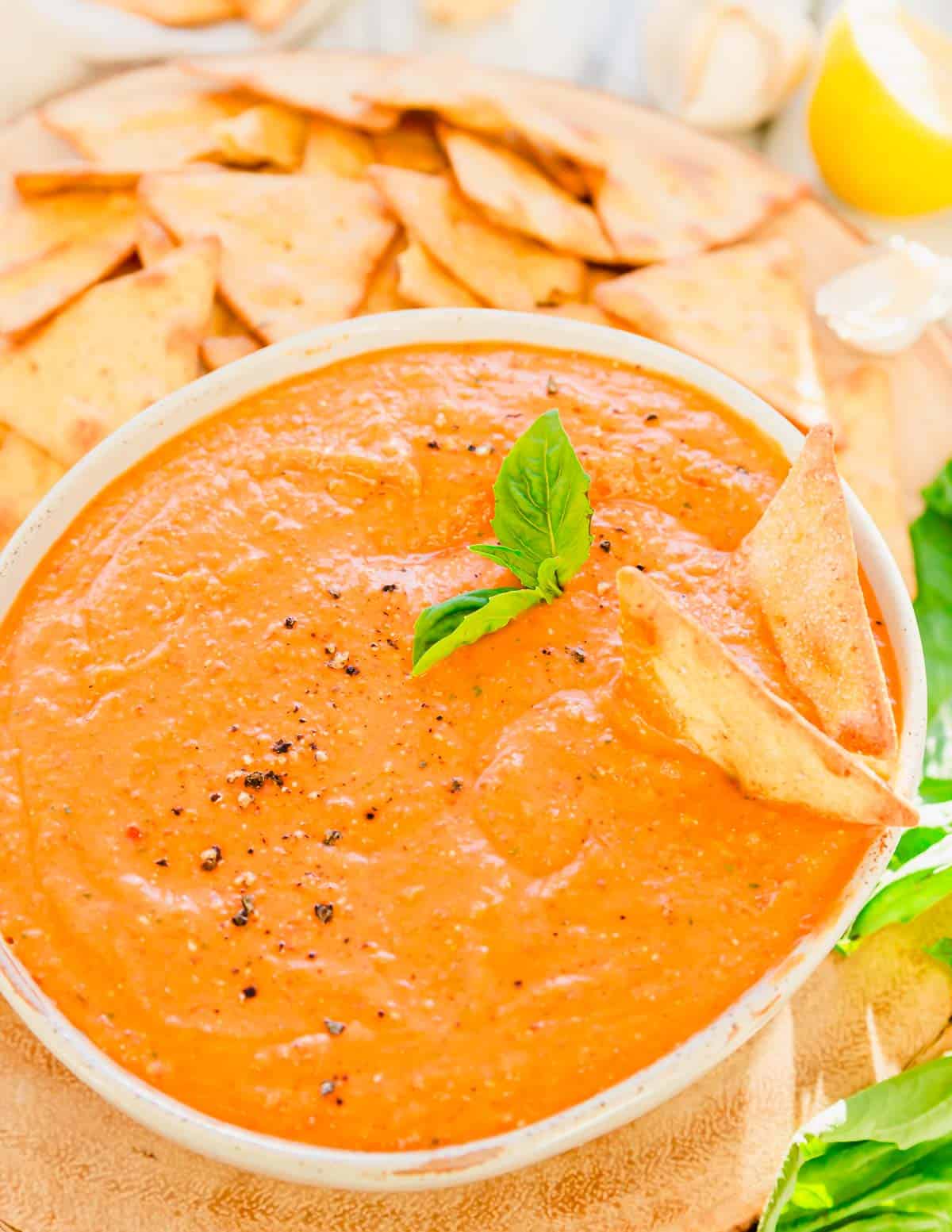 Two crackers in a bowl of roasted red pepper dip with beans and feta.