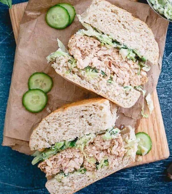 Chicken burgers and cucumbers on a wooden cutting board.