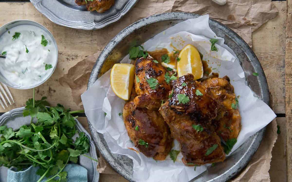 Indian spiced chicken thighs on a metal plate with lemon wedges.