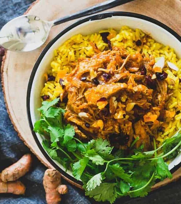A bowl of coconut pulled pork and turmeric rice on a wooden table.