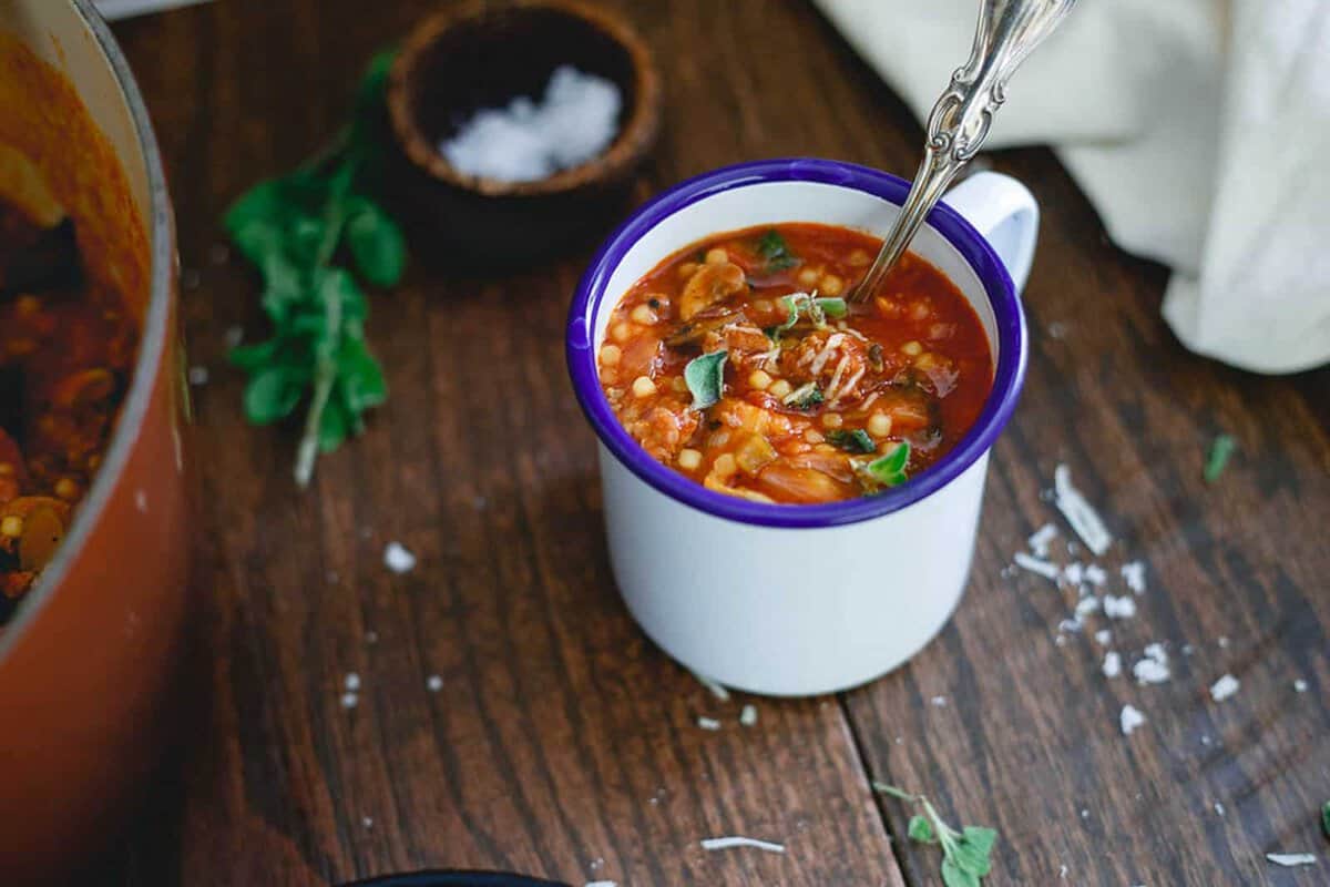Italian tomato soup with pasta in a mug with a spoon.