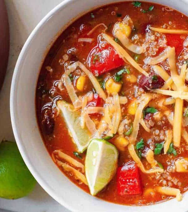 A bowl of mexican chili soup with corn tortillas and limes.