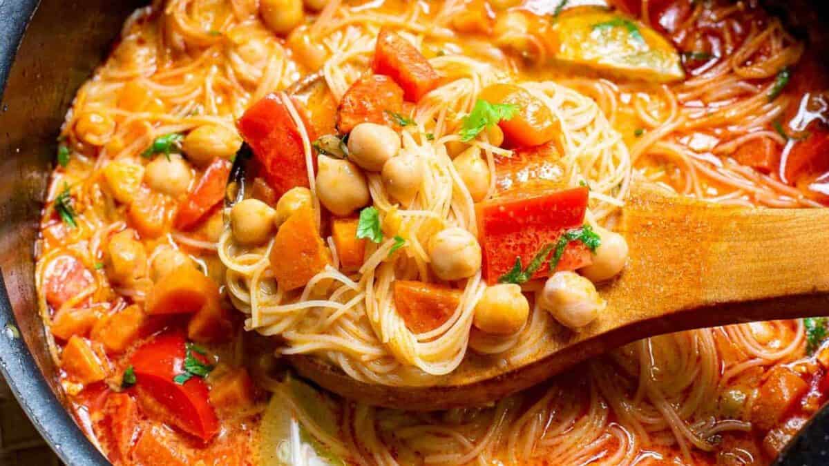 A pot of soup with noodles, tomatoes and chickpeas.