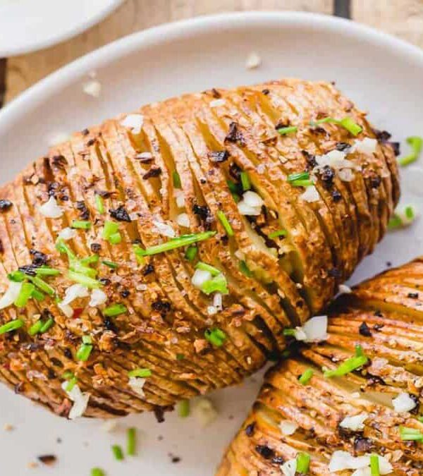 Two hasselback potatoes on a plate with salt and chives.