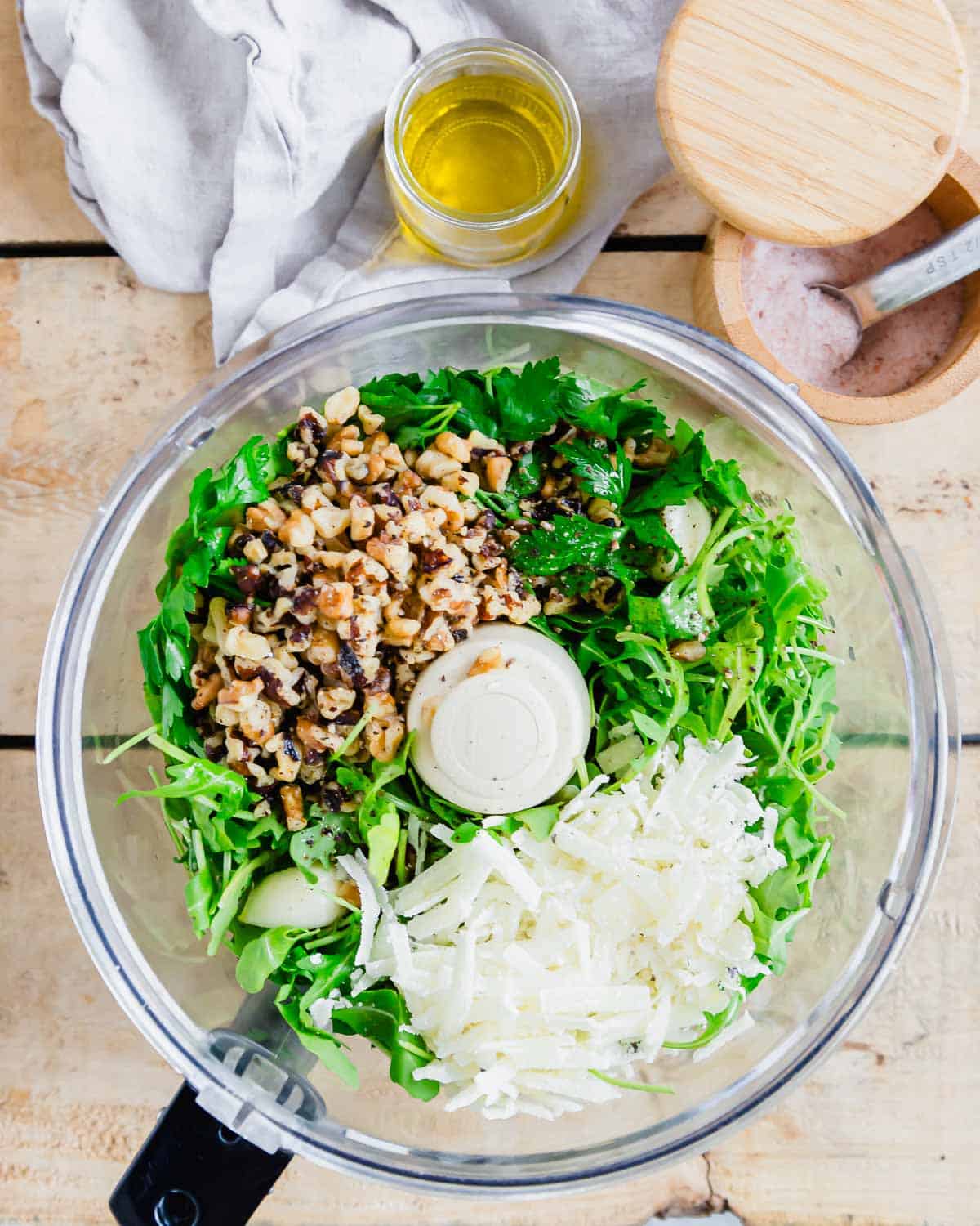 A food processor filled with ingredients for making pesto.