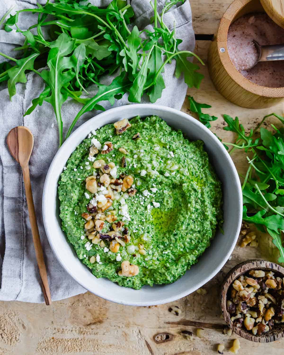 A bowl of arugula pesto with walnuts and crumbled parmesan.