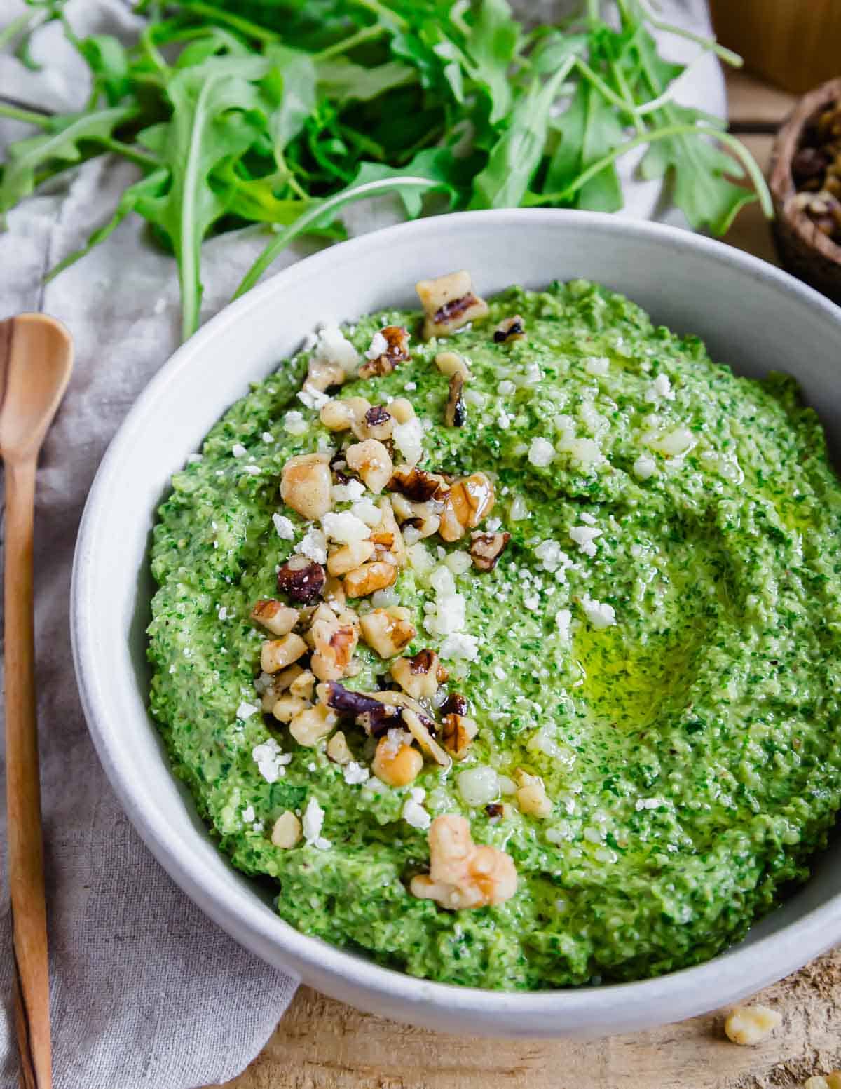 Close up of a bowl of pesto made with arugula with walnuts and grated parmesan.