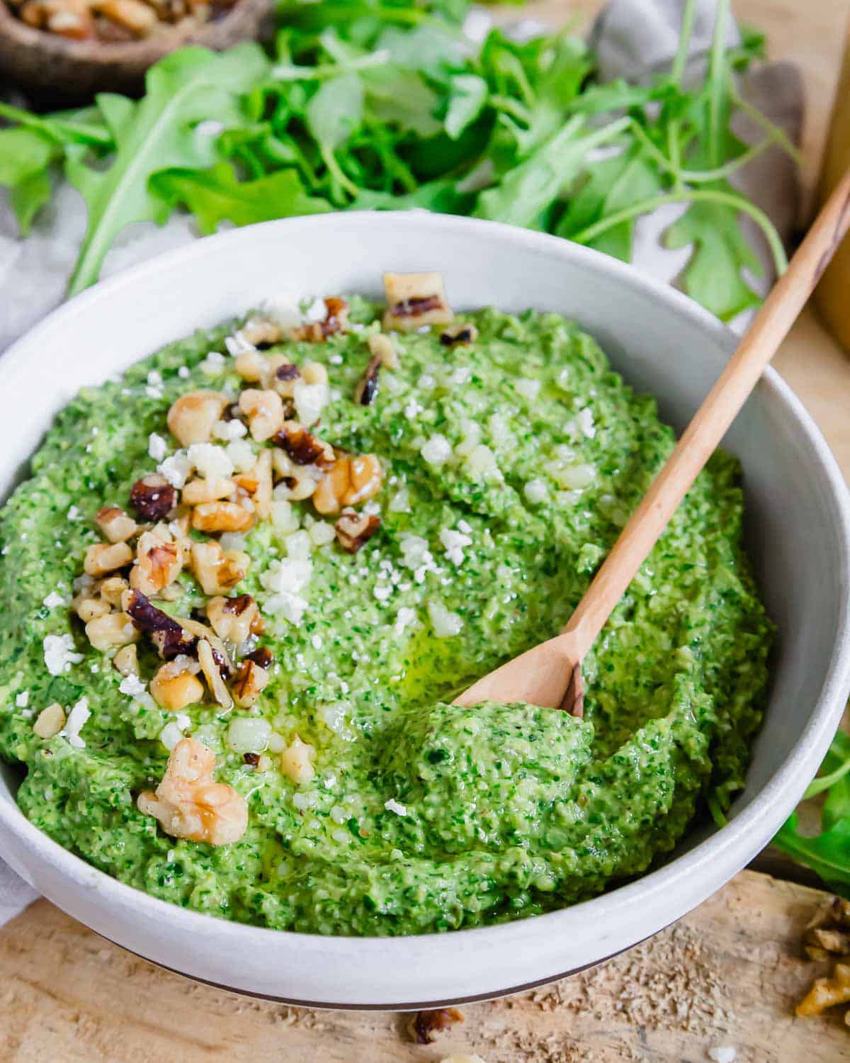 A small wooden spoon in a bowl of pesto.