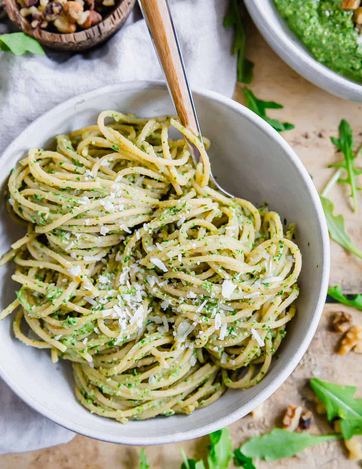 A bowl of spaghetti tossed with arugula pesto wrapped around a fork.