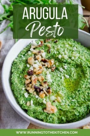 A bowl of arugula pesto garnished with walnuts and parmesan.