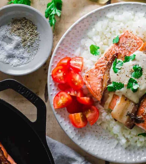 Salmon in a skillet with sauce and vegetables on a wooden table.