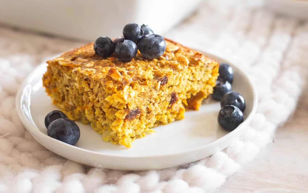 Turmeric baked oatmeal slice on a white plate with fresh blueberries.