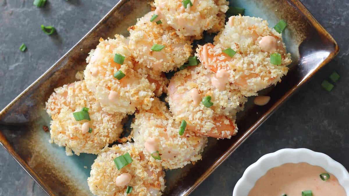 Baked bang bang shrimp on a serving plate garnished with green onions and served with dipping sauce.