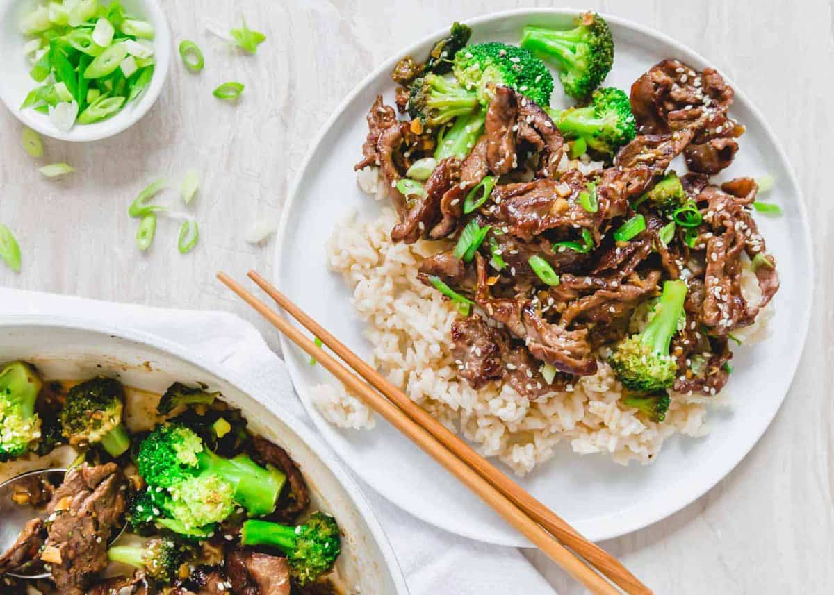 Beef and broccoli stir fry served with white rice on a white plate.