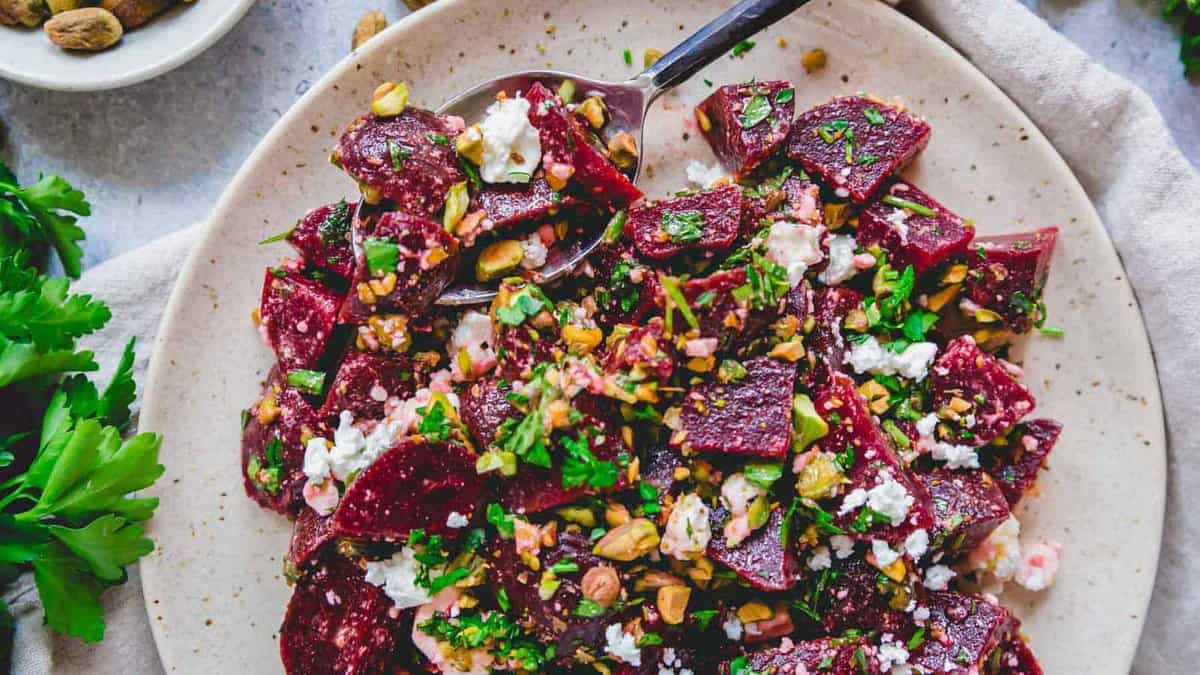 Beet salad with crumbled feta, pistachios and fresh herbs on a plate with serving spoon.
