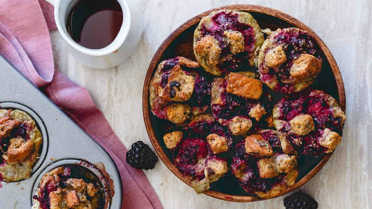 Blackberry ginger French toast bites on a wooden plate with maple syrup on the side.