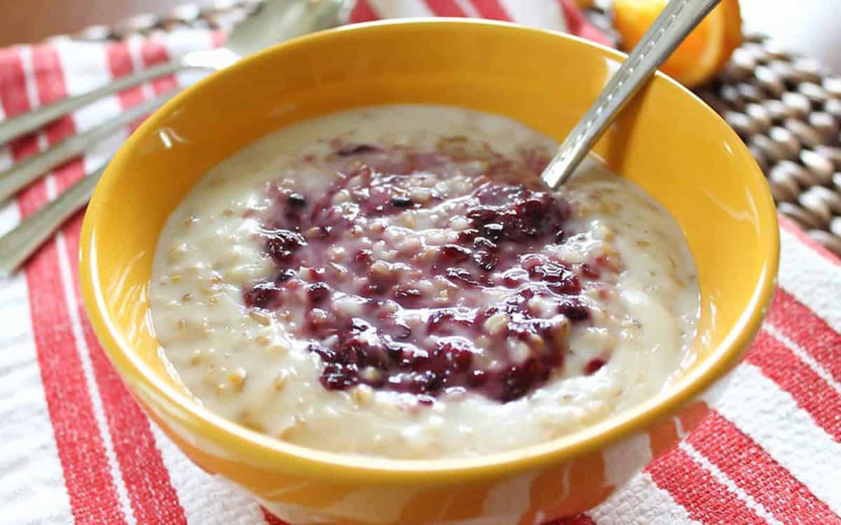 Orange steel cut oats in a yellow bowl with blackberry sauce swirled in the center.