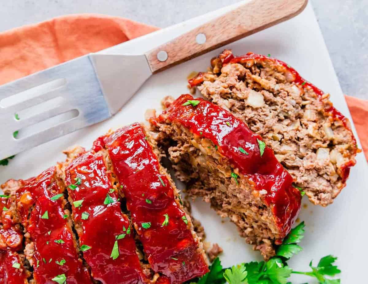 Meatloaf on a white plate cut into slices with fresh parsley garnish.