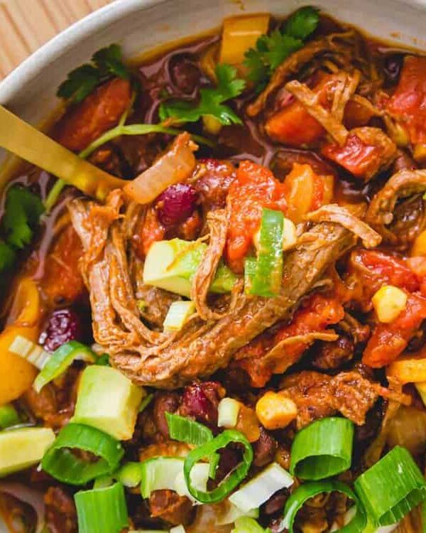 A bowl of beef brisket chili with vegetables and avocado.