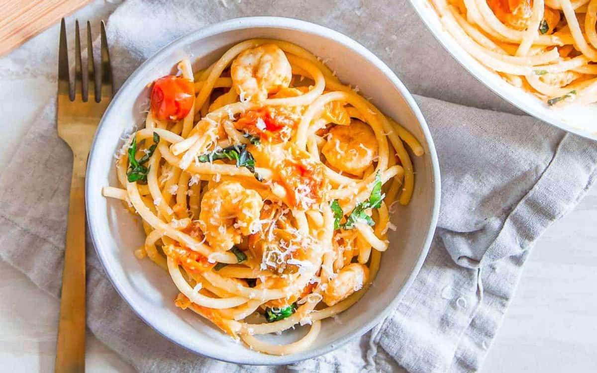 Bucatini pasta with shrimp in a white bowl.