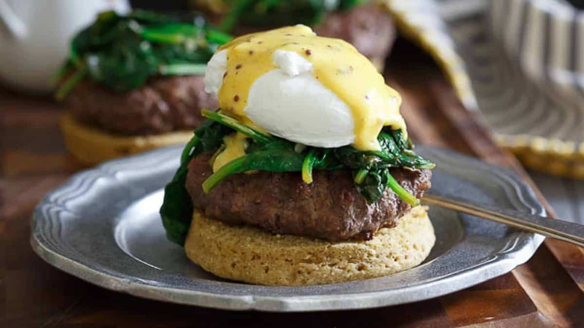 Open faced burger eggs benedict on a metal plate with a fork.