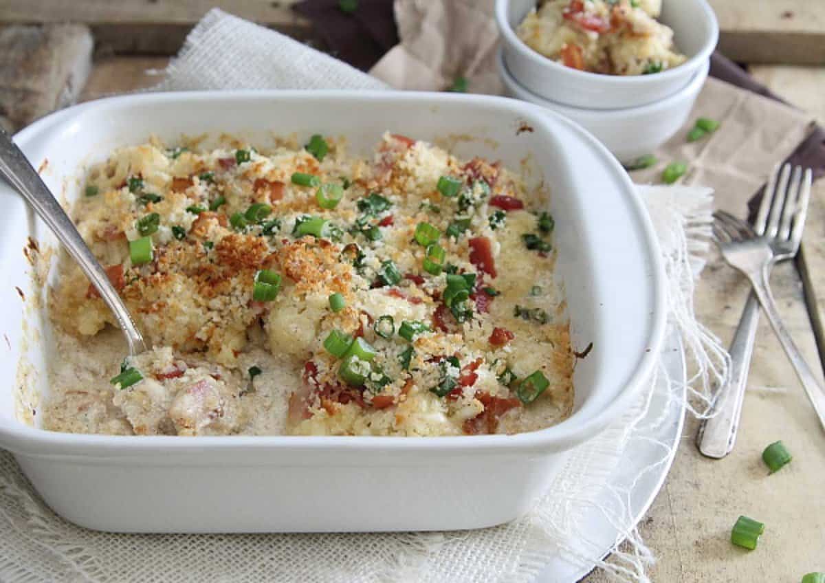 Cauliflower bacon gratin in a white baking dish with serving spoon.
