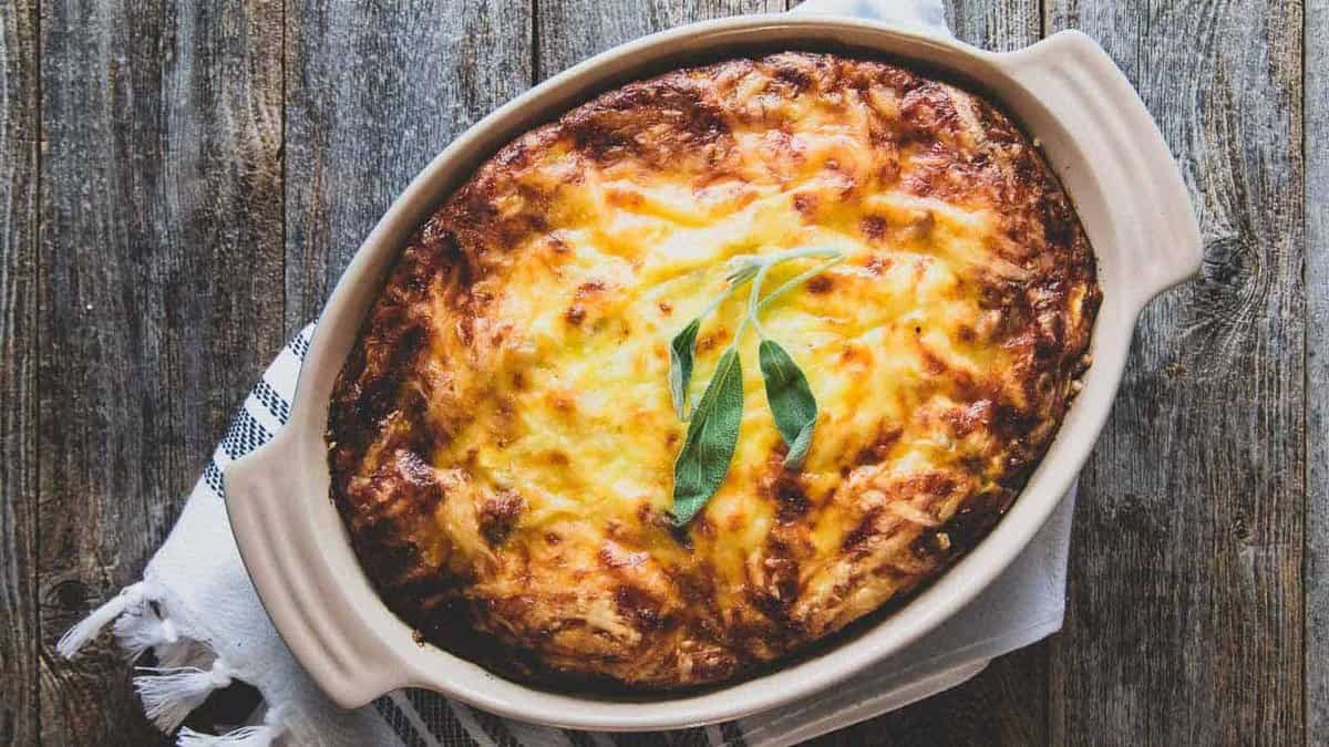 Cheesy potato and sausage casserole in a baking dish on wooden surface.