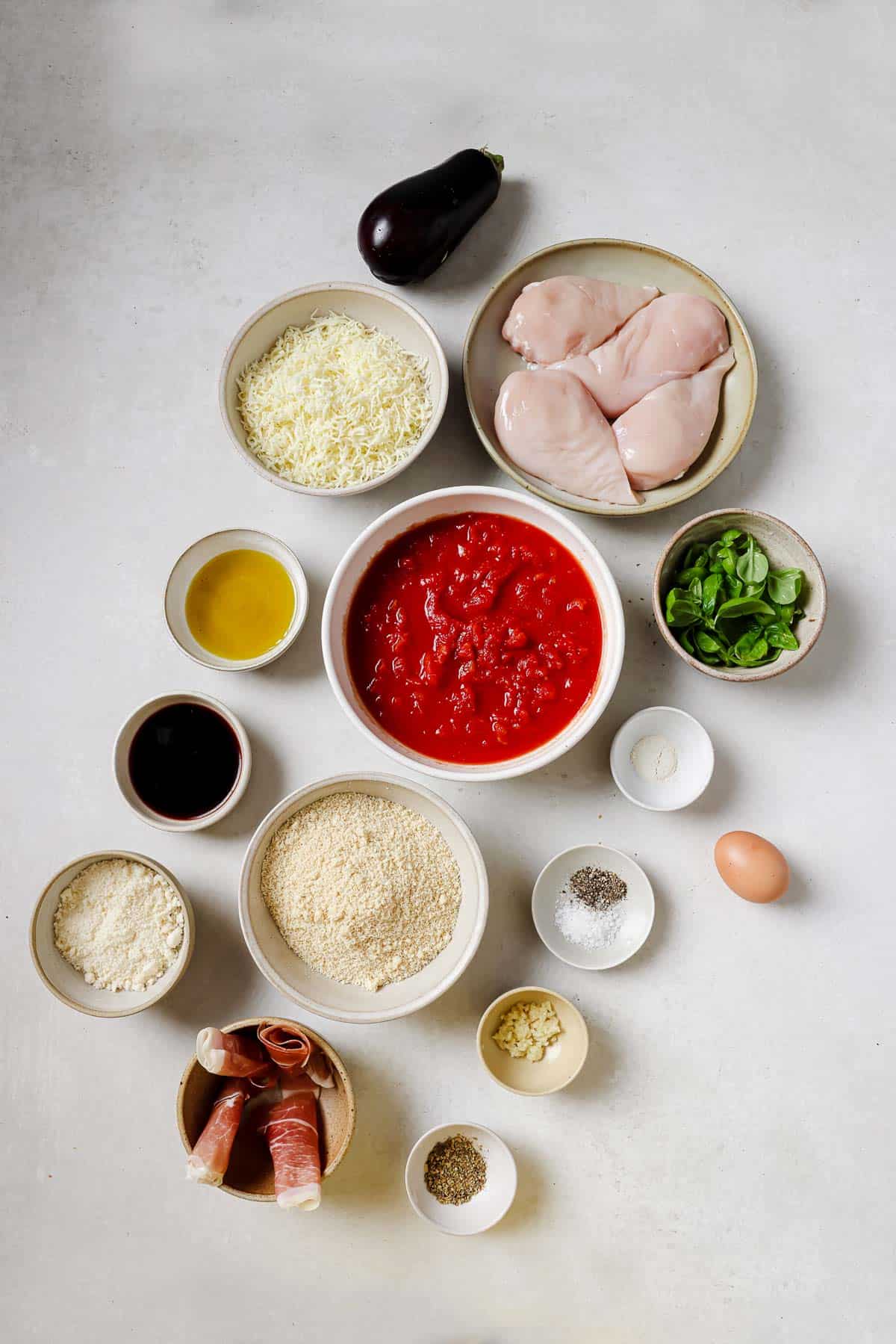 The ingredients for making a chicken sorrentino recipe are laid out on a table in bowls.