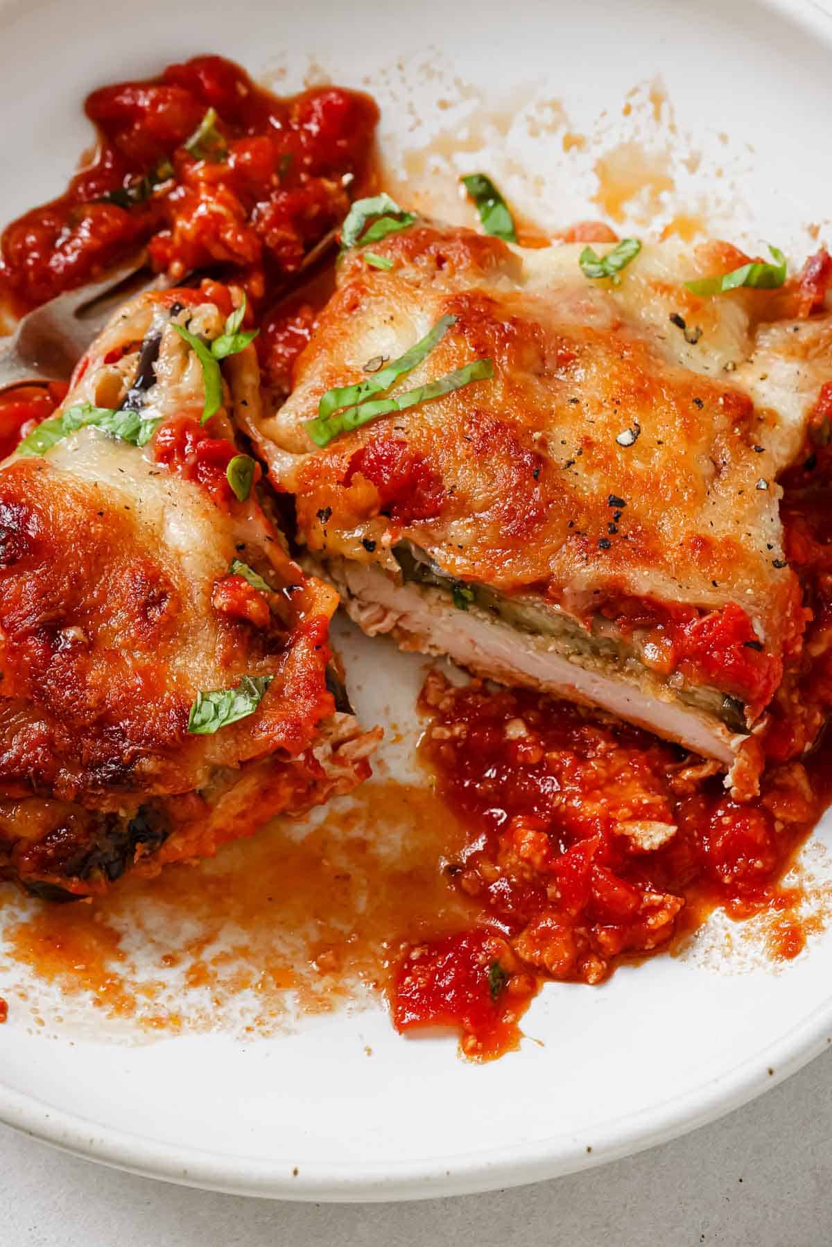 Chicken Sorrentino cut in half on a plate with extra sauce.