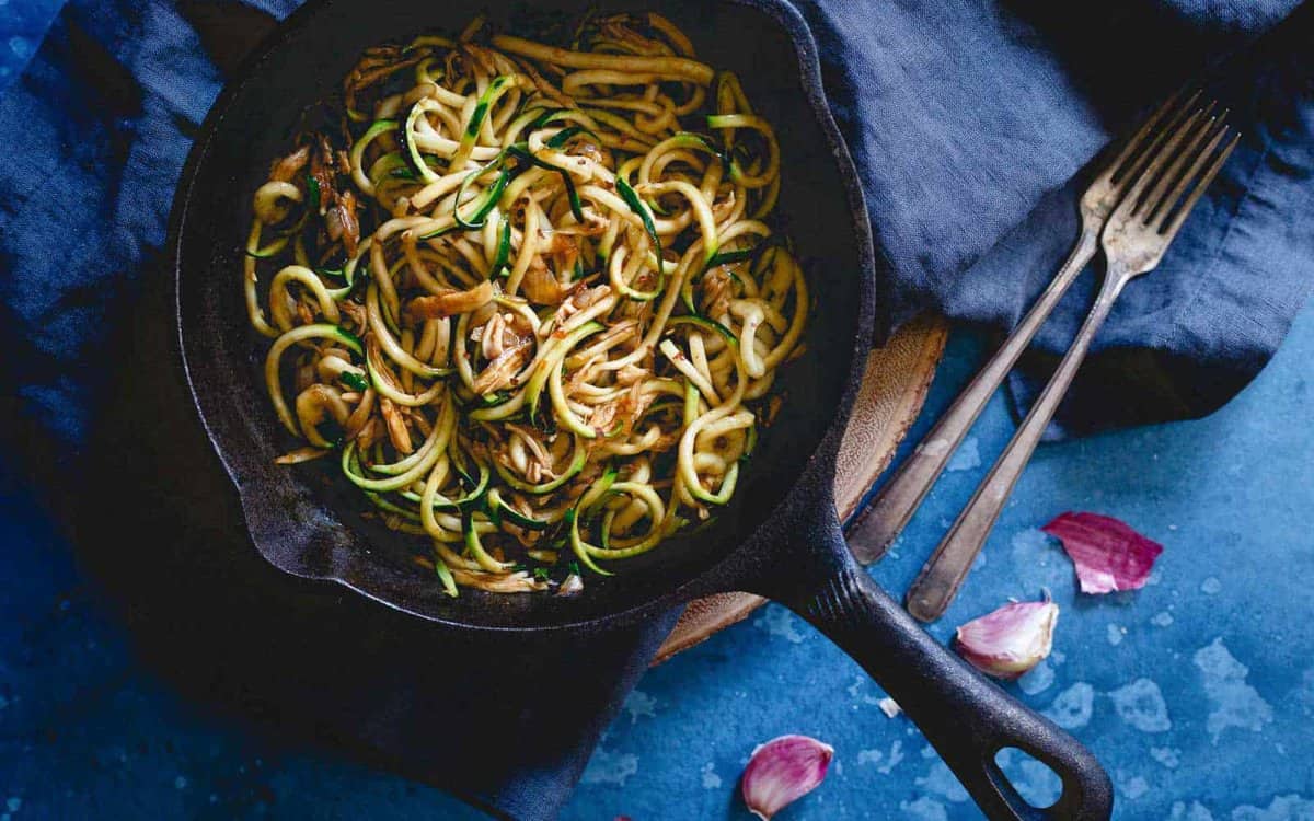 Zucchini noodles with shredded chicken in a stir fry sauce in cast iron skillet.