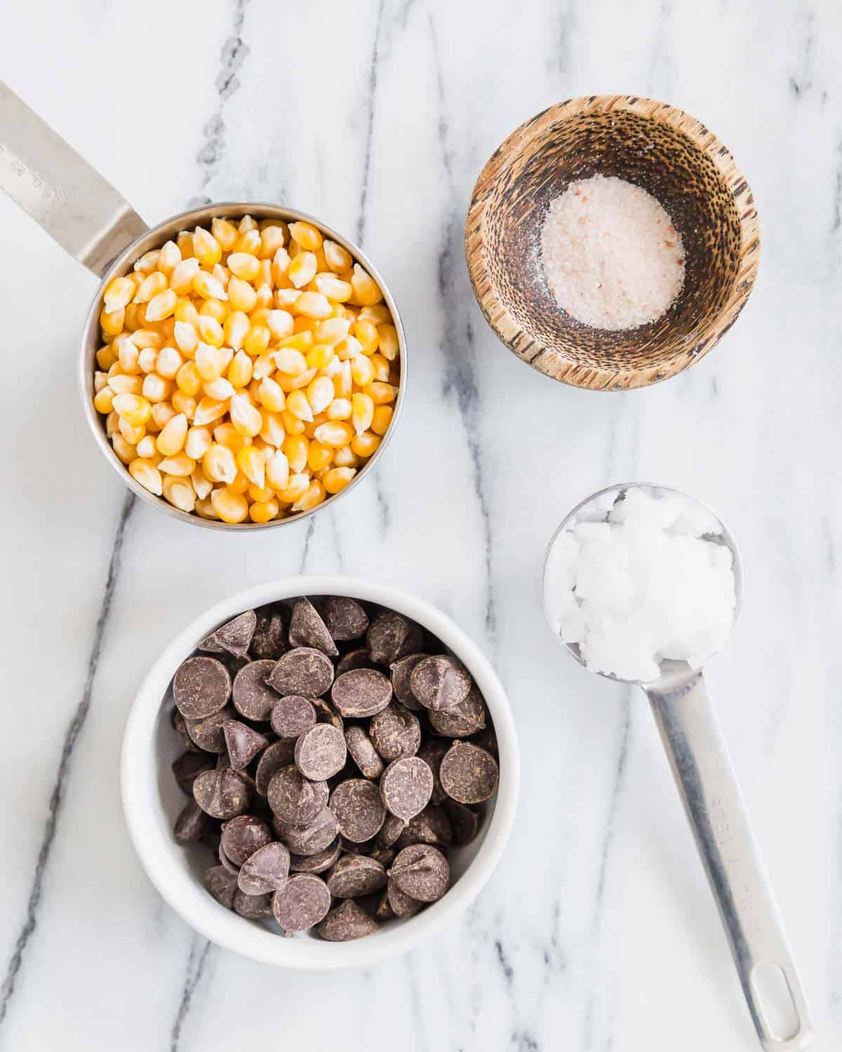 A bowl of chocolate chips, popcorn and salt on a marble countertop.