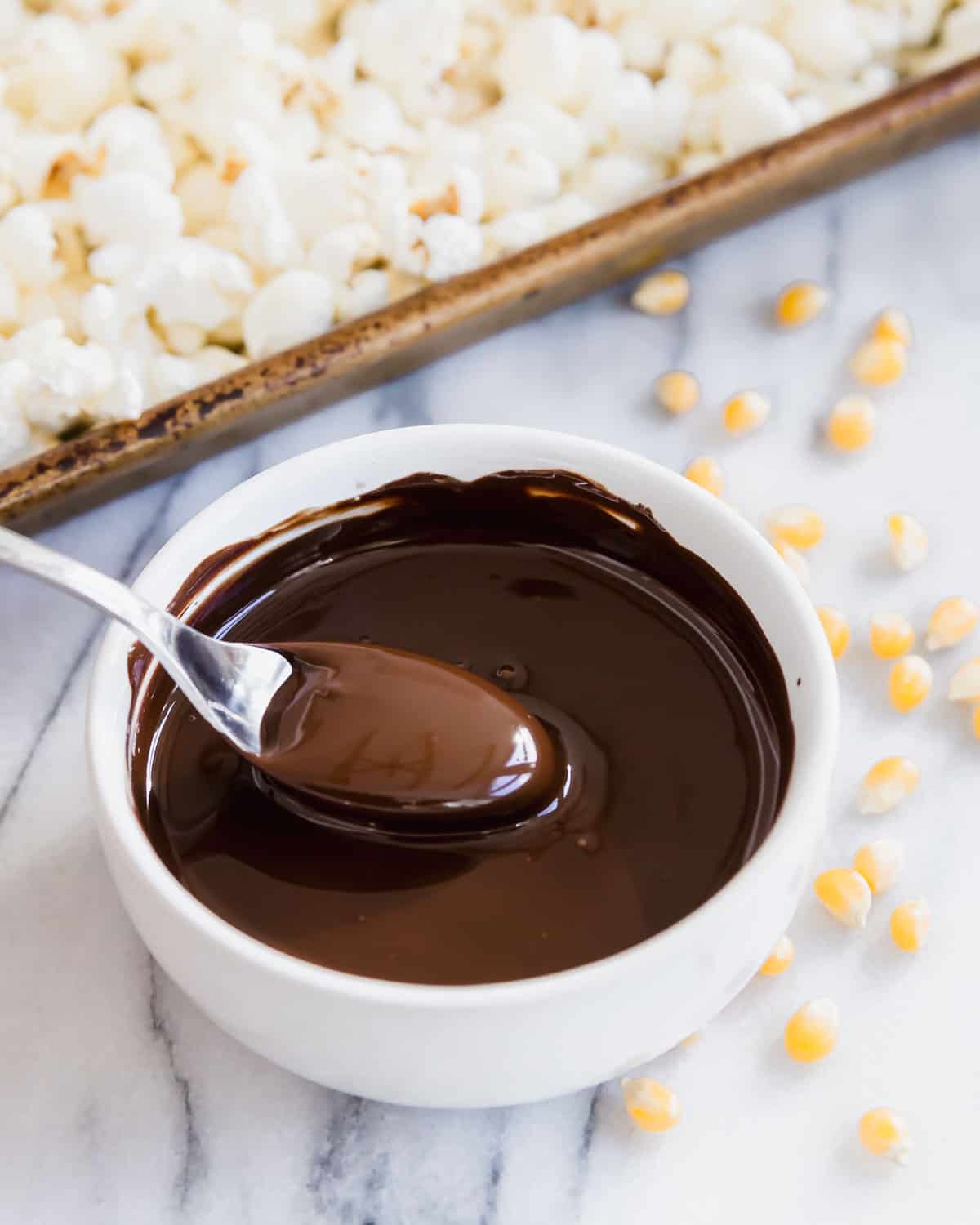 A baking sheet full of popcorn with chocolate sauce and a spoon.
