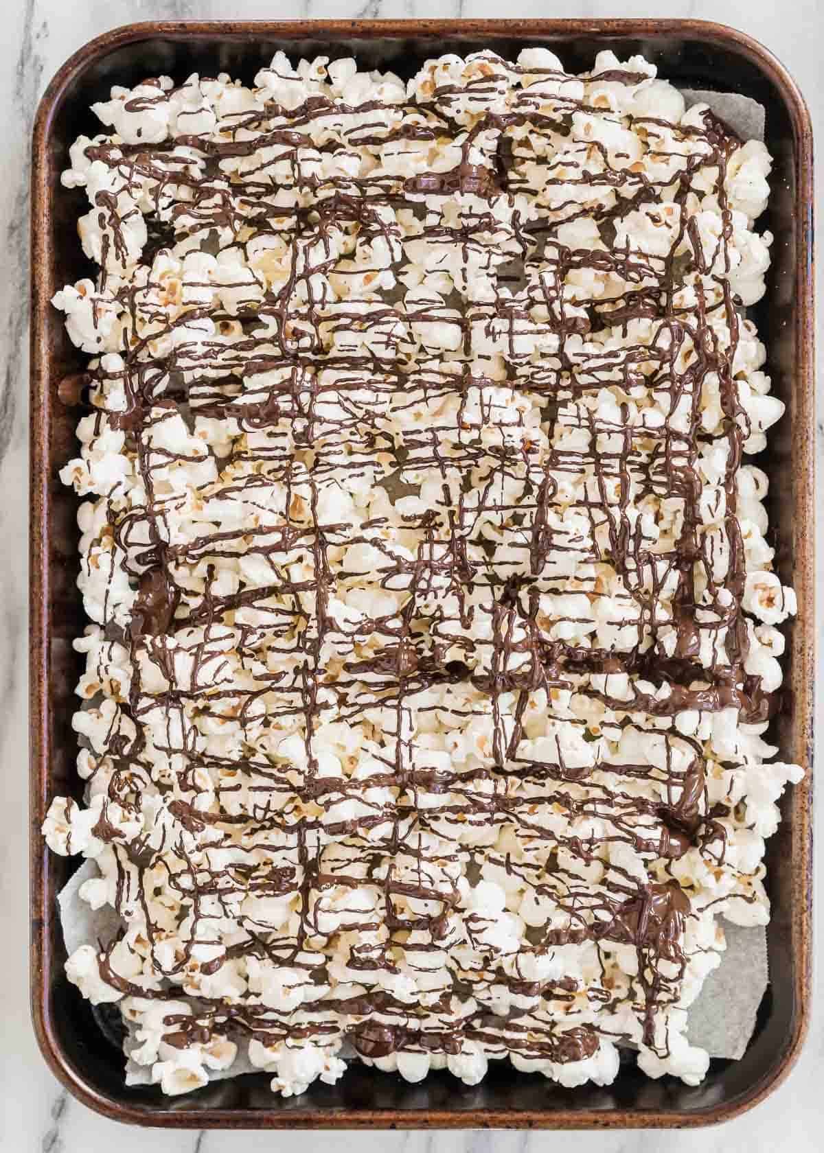 Chocolate drizzled popcorn in a baking pan.