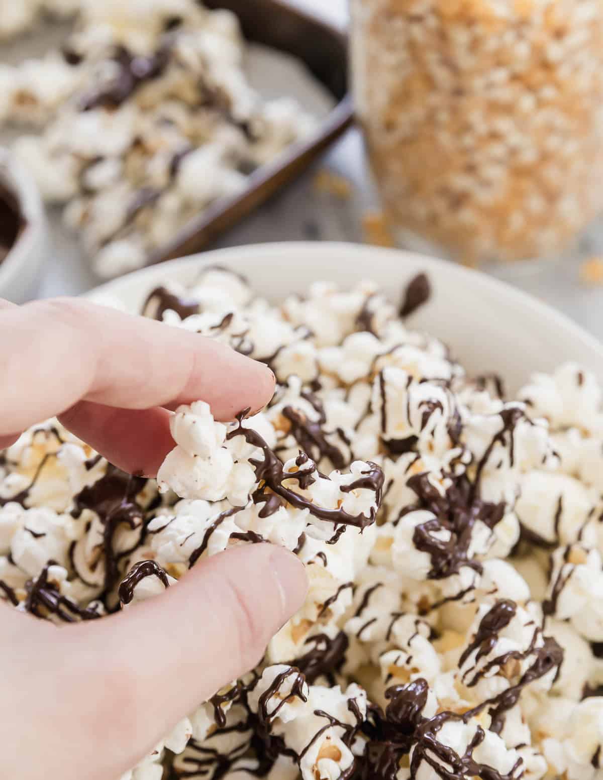 A person is dipping a hand into a bowl of popcorn with chocolate drizzle.