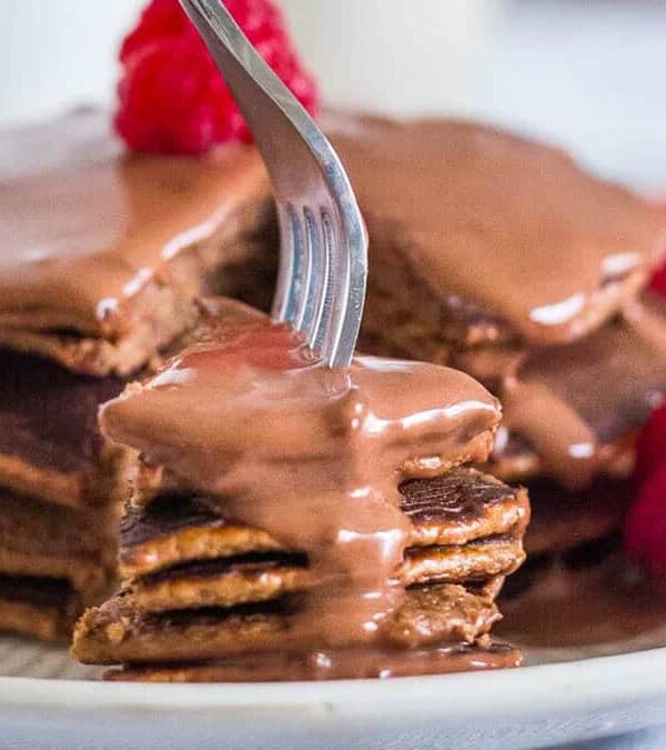 A stack of pancakes with chocolate sauce and raspberries on a plate.
