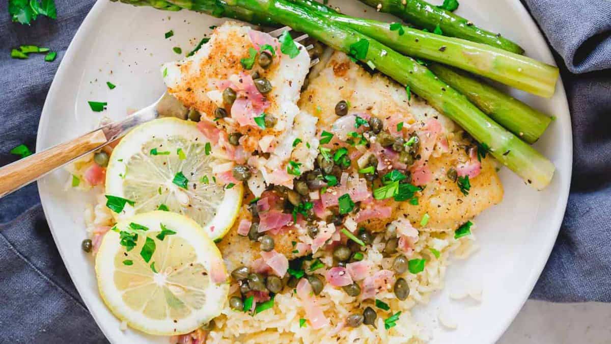 Cod piccata on a plate with asparagus and rice.